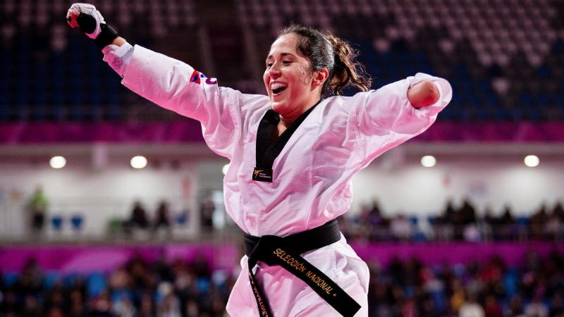 a female Para taekwondo athlete raises her arms in celebration