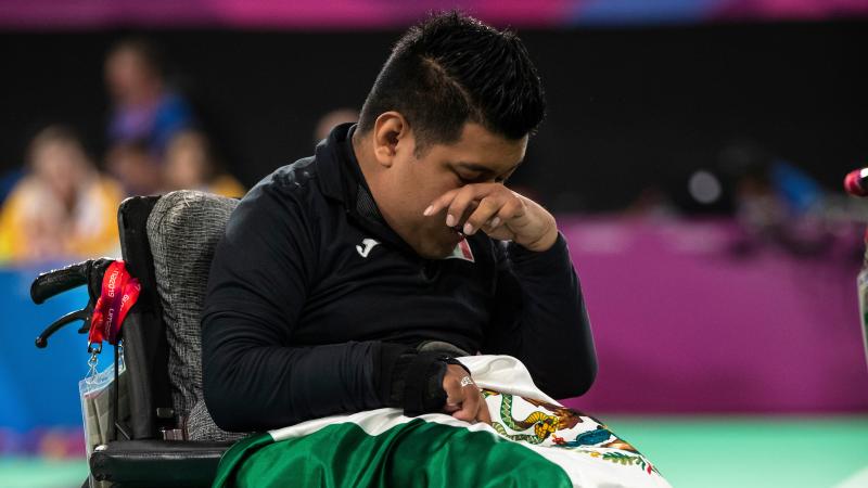 a male boccia player wipes away a tear with the Mexican flag on his lap