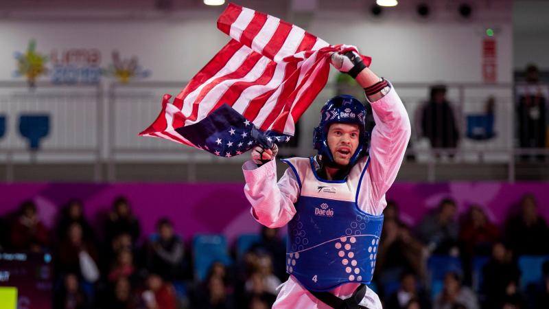 a male Para taekwondo fighter holding up the USA flag