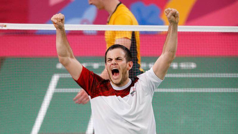 a male Para badminton player raises his arms into the air in celebration