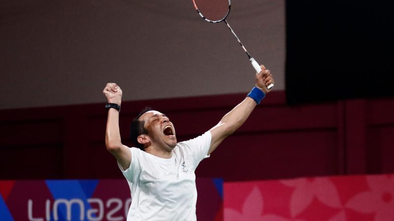 a male Para badminton player raises his fist and racquet into the air in celebration