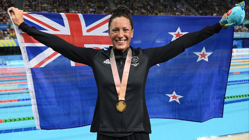female Para swimmer holding up a New Zealand flag