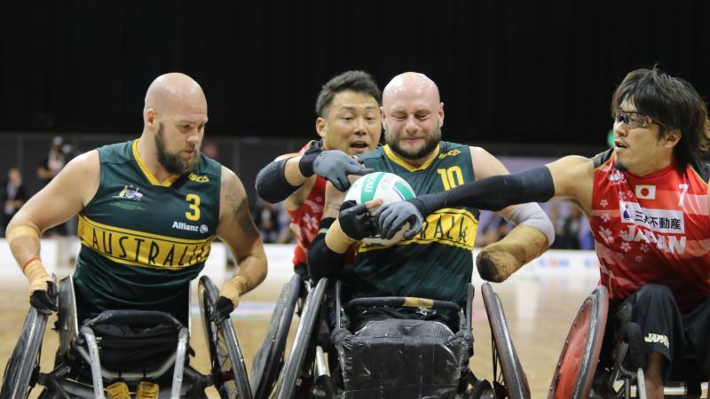 Man tries to hold onto wheelchair rugby ball while defenders surround him