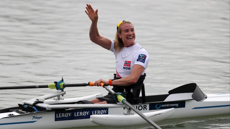 Woman in rowing boat waves at spectators