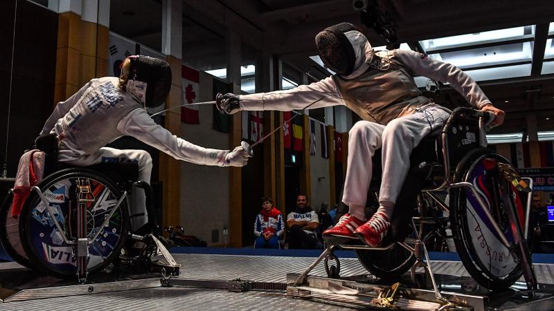 Two wheelchair fencers reach to strike their opponent