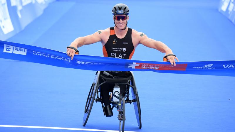 Man in racing chair smiles crossing finish line tape