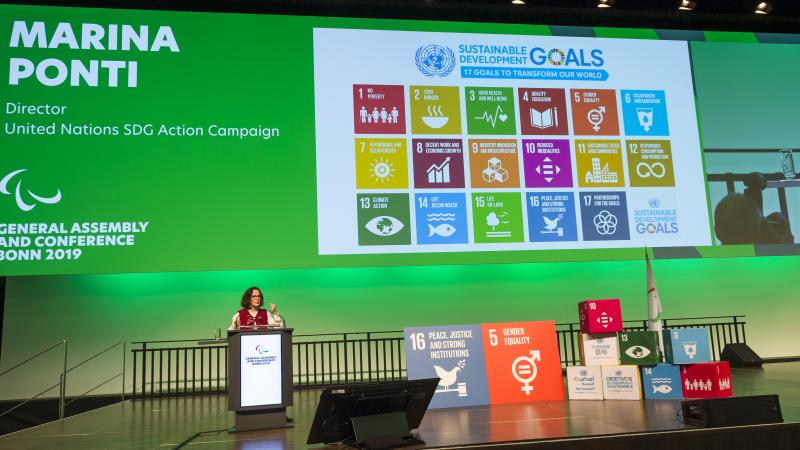 A woman on a stage making a presentation about the UN SDGs