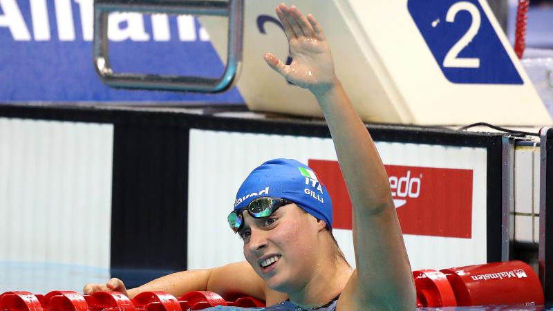 A female swimmer in the swimming pool waving