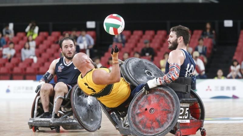 Two wheelchair rugby players knock over an opponent