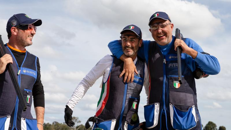 Two Italian shotgun athletes have arms around each other laughing 
