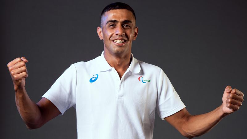 A man smiling to camera wearing a white shirt with the Agitos