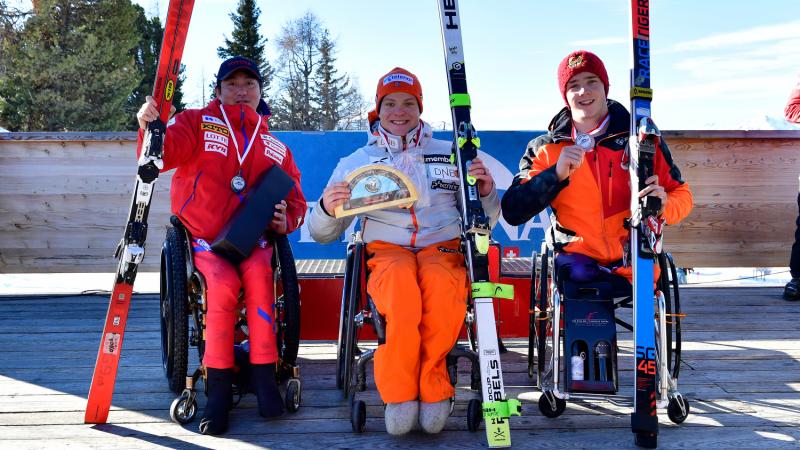Three male sit skiers pose on the podium