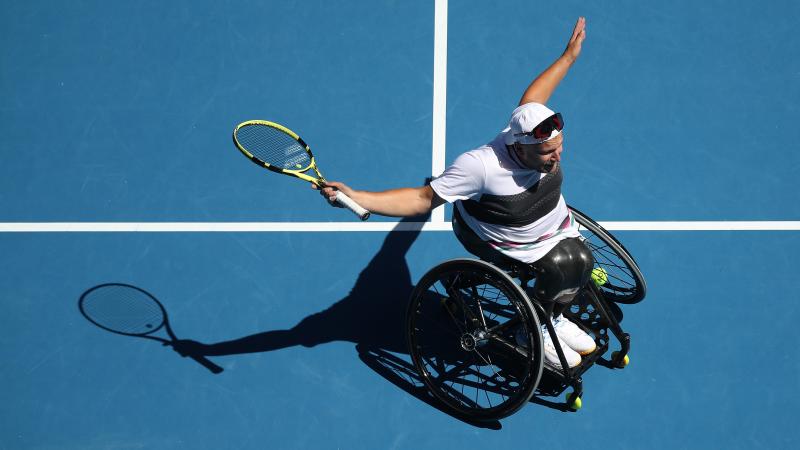 Dylan Alcott on the court extending his arms in celebration while holding the racket