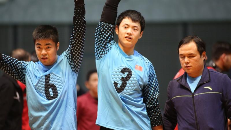 Chinese goalball players lift their arms after a victory