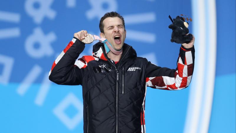A man celebrating and showing his bronze medal on the podium 