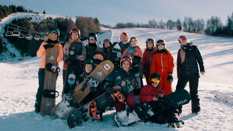 A group of 12 female Para snowboarders posing for picture with their equipment on the snow