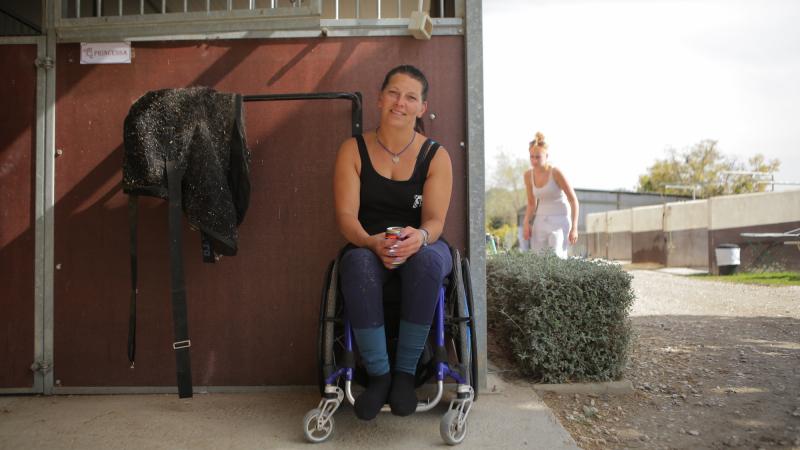 Woman in wheelchair smiles outside a horse stable