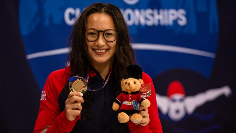 A woman wearing glasses showing her gold medal 