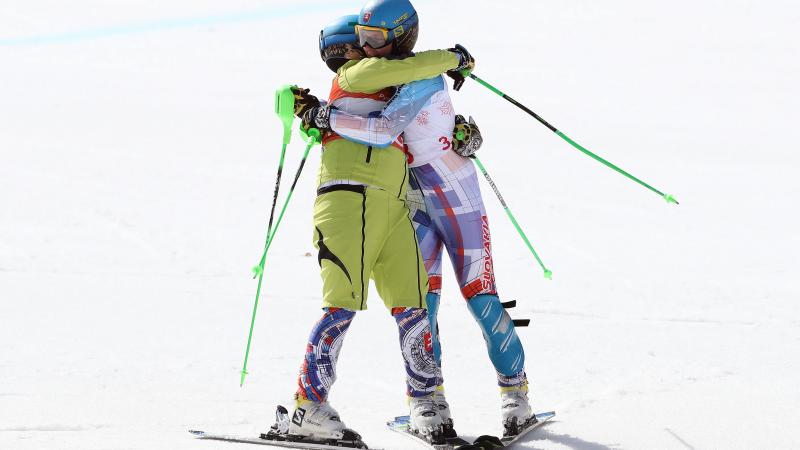 Two male alpine skiers hugging each other on the snow