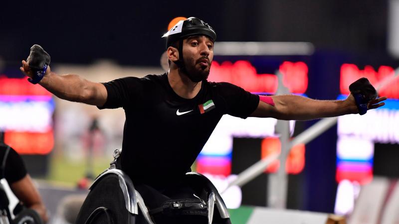 A man in a racing wheelchair celebrating with his arms stretched 