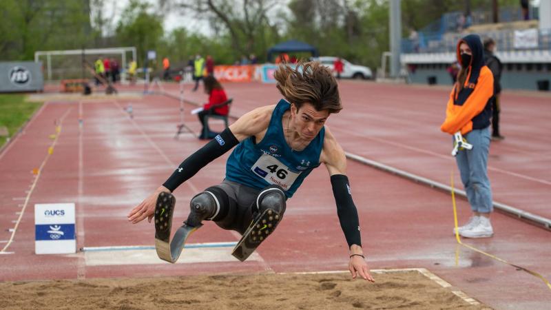 A men with prosthetic legs competing in a long jump event observed by a female official