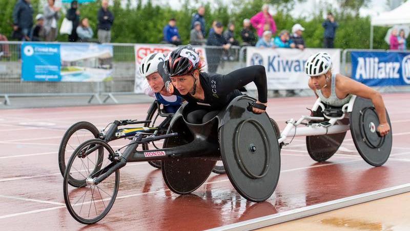 Three female wheelchair racers competing on a track under rain