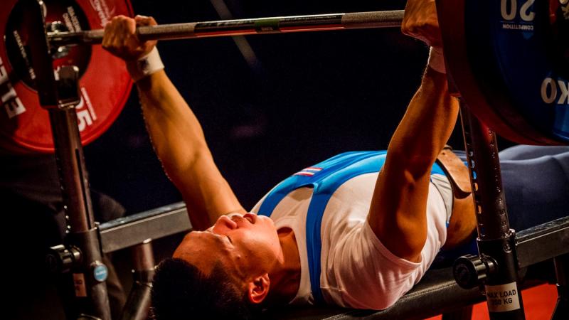 A man on a bench press lifting a bar in a Para powerlifting competition