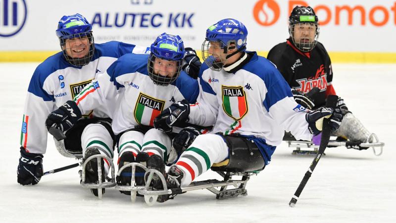 Three Para ice hockey players with the uniform of Italy celebrating with another player from Japan observing