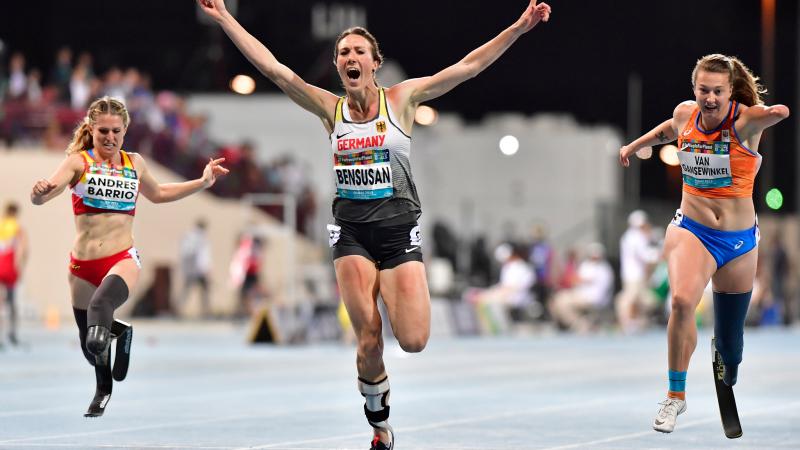 A female athlete celebrating after finishing a race ahead of two other women with prosthetic legs