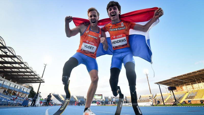 Two male sprinters with prosthetic legs celebrating with the flag of Netherlands