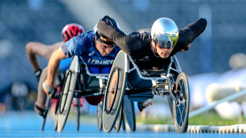 A men in a racing wheelchair leading a competition being followed by two competitors
