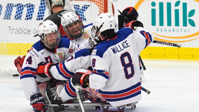 Three USA Para ice hockey players hugging during a game on an ice rink