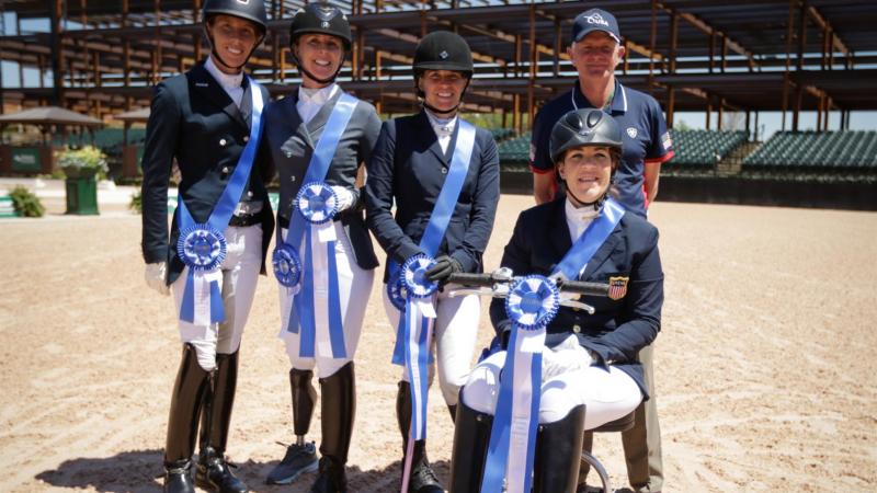 Female equestrian riders pose for a photo with their male coach in the back