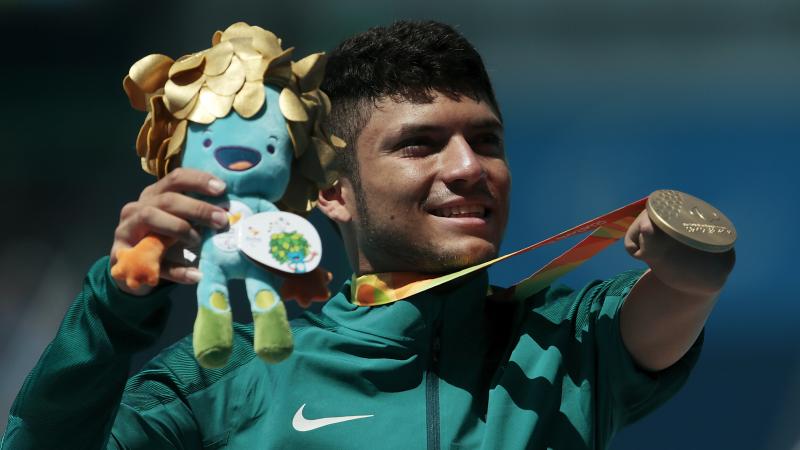 A man without an arm holding a mascot and showing his gold medal