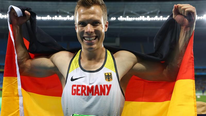 An smiley athlete holding the German flag behind his back