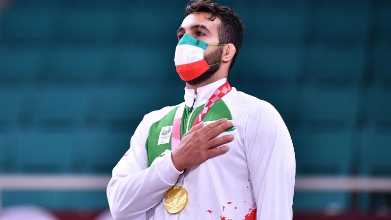 Iranian judoka Vahid Nouri with his gold medal hanging around his neck and his hand on his chest while listening to the Iranian national anthem