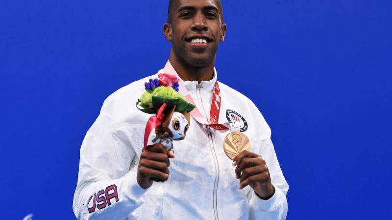 A man with the uniform of USA on a podium holding his medal 