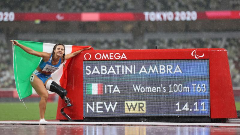 A woman with a prosthetic leg standing next to a screen showing her name and record on an athletics track