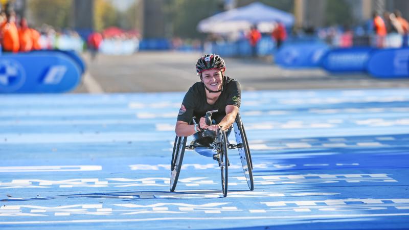 A female wheelchair racer smiling crossing the finish line on a street race