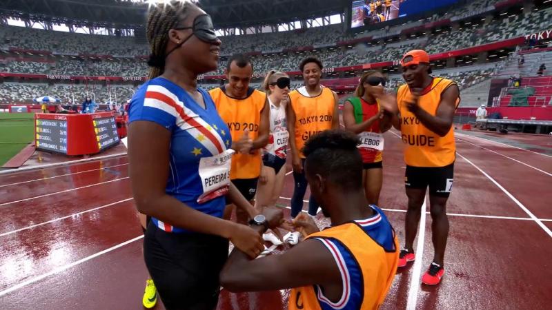 A man kneeling on an athletics track to propose a female athlete surrounded by four people