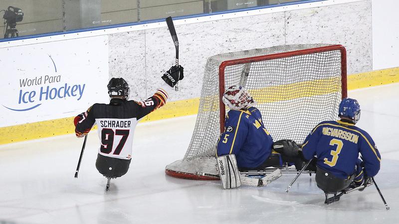 A German Para ice hockey player celebrating against two Swedish players on an ice rink