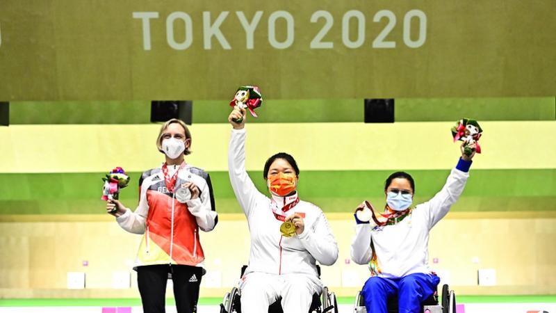 A woman standing next to two female wheelchair users on a podium at Tokyo 2020