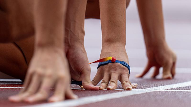 Two pairs of hands side by side on an athletics track starting line