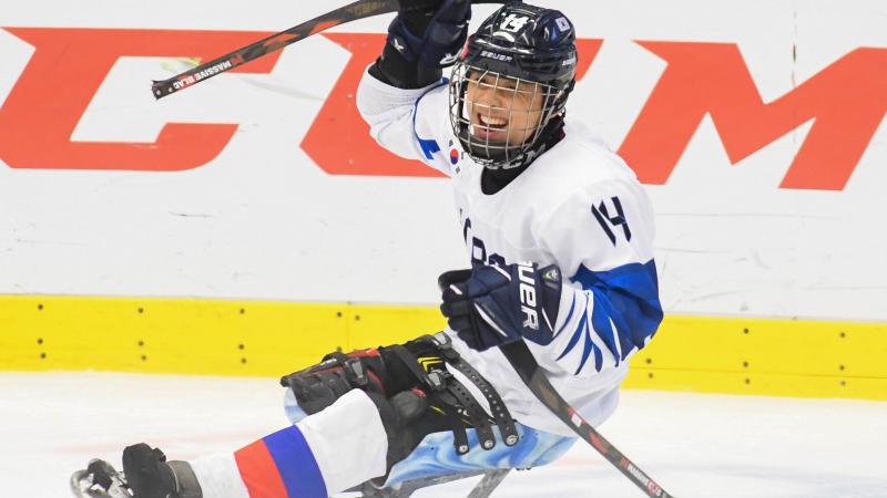 A Para ice hockey player on a sledge celebrates with his right arm raised.