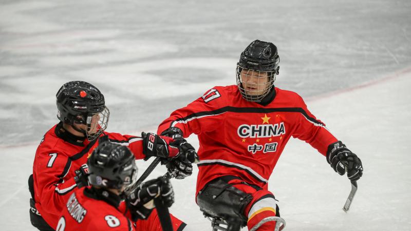 Three Para ice hockey players in red jerseys celebrating with fist bumps.