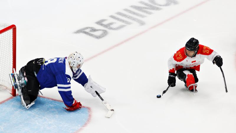 A Para ice hockey player moves past the goalie navigating the puck with a stick.