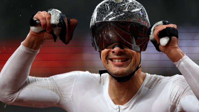 Switzerland's Marcel Hug wears a silver helmet that is shining with rain droplets and raises his hands to celebrate his victory in the men’s 800m T54 final