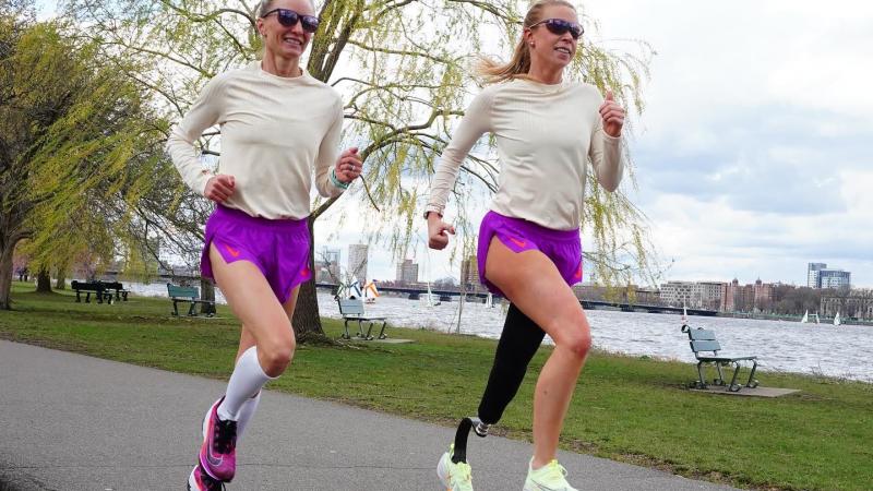 Adrianne Haslet and Shalane Flanagan wear matching beige and purple outfits as they run along the bay during training for the 2022 Boston Marathon.