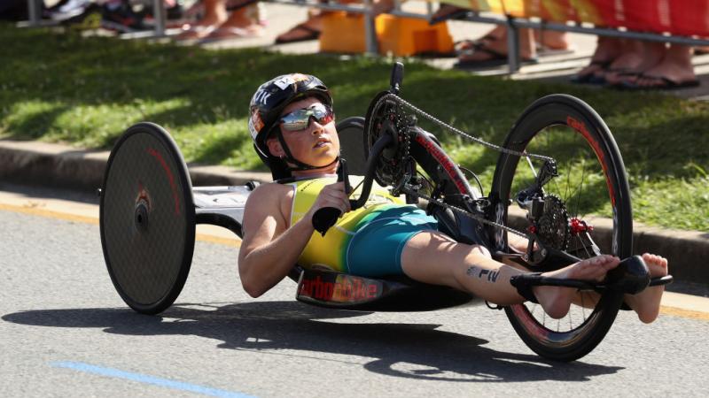 Lauren Parker, wearing the Australian kit but no shoes, rides her handbike on a cement road during the women's PTWC final at the 2018 Commonwealth Games.