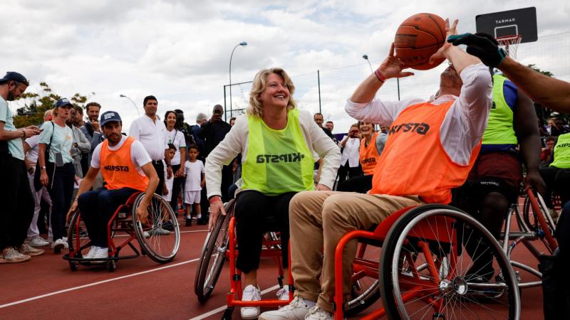 One woman and two men try out wheelchair basketball surrounded by spectators.